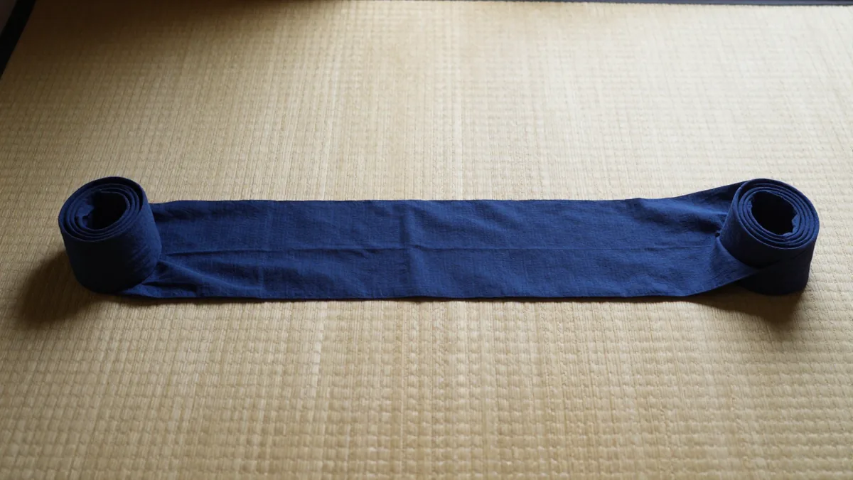 両端を巻いて畳の上に伸ばした、藍色の細長い帯