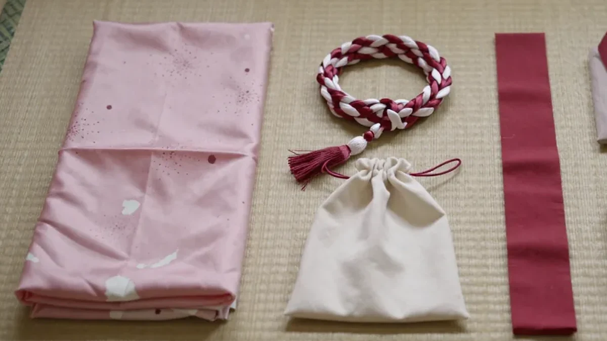 畳の上に並べたピンクの布、紅白の組紐、白い巾着、赤い細長い布